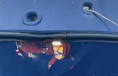 Reflection of a person in orange attire on the shiny surface of a blue structure.