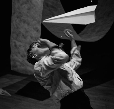 A person in a white shirt is interacting with a large paper plane in a dimly lit room.