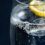 Close-up of a glass of sparkling water with ice and a slice of lemon, showing bubbles rising to the surface against a dark background.