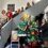 A group of people in festive clothing pose beside a Christmas tree made of knit hats on a staircase indoors.