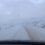 Snow-covered road with a wind turbine in the background, surrounded by a snowy landscape and overcast sky.