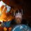 Person in Viking costume holding an axe and shield, standing in front of a large fire at night.