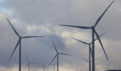 Wind turbines under a cloudy sky, blades spinning gently in a field.