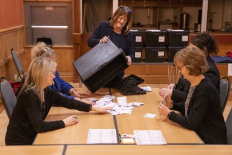 A woman empties a ballot box onto a table while four other people sort through the papers.