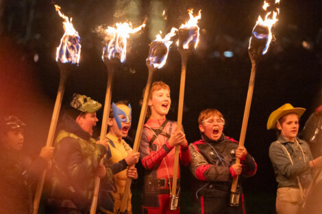 Children in costumes holding flaming torches, standing in a line.