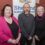 Three people standing in front of a Shetland Islands Council banner inside a room with wood-paneled walls.