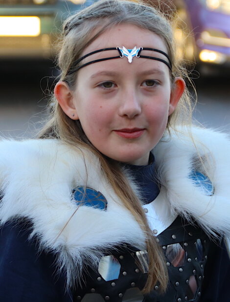 A person wearing a fur-trimmed outfit, blue attire, and a headband with a butterfly design.