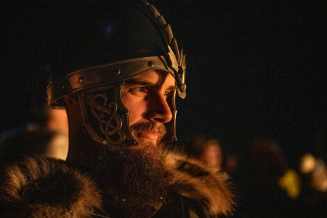 A person wearing a detailed metal helmet with fur-lined clothing, illuminated by a warm light source.