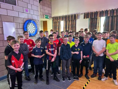 A group of boys posing indoors, some wearing sports jerseys, with a dartboard in the background.