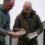 Two men examining samples in clear plastic bags outdoors, standing near industrial buildings.