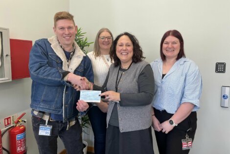 A person hands over a check to a woman while three other individuals stand nearby in an indoor setting.