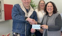 A person hands over a check to a woman while three other individuals stand nearby in an indoor setting.