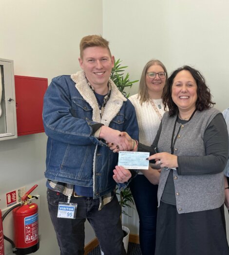 A person hands over a check to a woman while three other individuals stand nearby in an indoor setting.