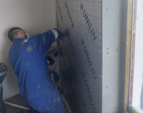 Person in blue coveralls installs insulation boards on a wall.