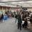 A busy indoor career fair with multiple booths, company banners, and people walking, talking, and seated at tables in a large, well-lit hall.