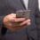A person in a suit holds a smartphone in one hand.