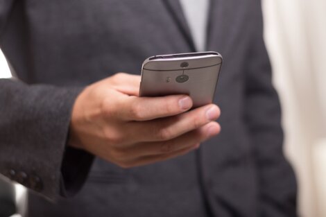 A person in a suit holds a smartphone in one hand.