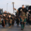 A group of people dressed in Viking-style costumes parade down a street, some carrying shields and axes, with adults and children leading the procession.