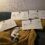Five large ceremonial checks for donations are displayed on a couch, with a cat lying on its back in front of them.