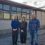 Three people stand in front of a fenced-off building on a sunny day. Two women are on the left and a man is on the right. The building has large windows and a pebble-dash exterior.