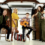 Four musicians pose in a garage with instruments: a violin, guitar, accordion, and an upright piano in the background. Three are standing and one is seated, all looking at the camera.