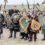 A group of people dressed in Viking costumes, holding shields and axes, stand outdoors in a celebratory pose with hills in the background.