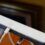 A close-up of a white tablet with a visible home button, connected to a charging cable on a wooden surface.