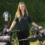 A woman stands outdoors holding a loaded touring bicycle with panniers and a cello case attached to the rear.