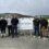 Seven men stand in front of a sign that reads "Welcome to the Gremista Grid Supply Point Project" at an outdoor construction or industrial site.