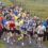 A group of runners at the starting line of a road race on a rural path, with marshals and spectators standing on the sidelines.