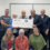 Ten people pose indoors, holding a large cheque for £400 from the Bank of Scotland with "Viking Genes Fund" written on it. Three people are kneeling in front, and seven are standing behind.