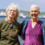 Two older women stand side by side outdoors near a body of water with boats and ships in the background on a sunny day.