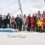 A group of sixteen people in sailing gear stand and pose together on the deck of a sailboat named "Ender Pearl.