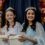 Three girls wearing dresses and tiaras sit with decorated background, smiling and holding white donation buckets.