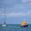 A lifeboat is towing a sailboat across calm blue water under a cloudy sky.