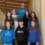 A group of eight people, including one adult and seven children, stand on an indoor stairway, posing for a photo. Most are wearing casual clothes or school-branded sweatshirts.