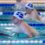 Two swimmers in a pool compete in a breaststroke race, both wearing swim caps with a blue and white flag design.