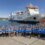 A large group of people in matching blue jackets pose for a photo on a dock in front of a NorthLink ferry on a sunny day.