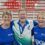 Three people stand smiling in front of a sign for the Scotland Disability Sport National Learning Games. The man in the center wears a medal and a blue shirt; the two women wear matching blue shirts.