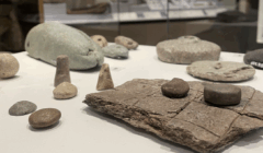 A display of ancient game pieces and a game board made of stone, featuring small carved stones and a rectangular board with a grid pattern, in a museum setting.