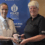 Two women in Police Scotland uniforms stand in front of a Police Scotland sign; one is handing a medal in a box to the other.