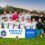 A men's football team celebrates behind a banner reading "Premier League Champions," with a trophy placed in front of them on a grassy field.