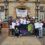 A group of people stand in front of a building holding banners that read "RECOVERY" and "Lived Experience Recovery Organisation." Some are wearing matching T-shirts and appear to be celebrating.