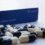 A close-up of black and white paracetamol 500mg capsules scattered in front of a blue box labeled "16 capsules.