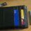 A black leather wallet with bank cards partially visible, next to a UK driving licence on a wooden surface.