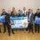 A group of people stands indoors holding a large "Fishing For Litter" banner, celebrating 20 years and 23,000 tonnes of marine litter removed from Scottish seas.