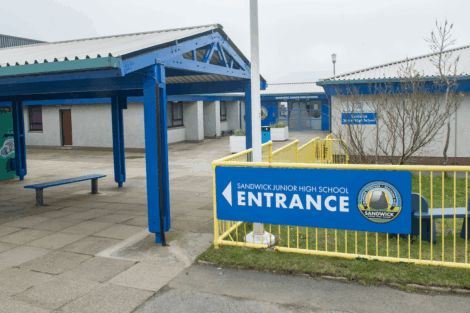 The main entrance of Sandwick Junior High School, with a blue sign and yellow railings in front of the building.