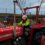 A child wearing a Santa hat and neon safety suit sits on a red Massey Ferguson tractor decorated with Christmas lights and tinsel, outdoors near a playground.
