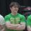 A young man with brown hair, wearing a green T-shirt with yellow lettering, stands with arms crossed and smiles.