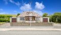 A detached grey-rendered bungalow with a central bay window, two brown garage doors, and a low lattice-topped front wall, set under a